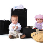 Two babies with their boarding pass surrounded by suitcases. The boy has his shoes in his hands. Isolated on white.