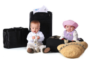 Two babies with their boarding pass surrounded by suitcases. The boy has his shoes in his hands. Isolated on white.